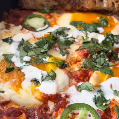 Masala shakshuka with eggs, cilantro and jalapeño in a skillet with toasted bread
