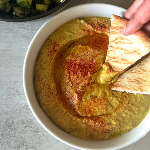 Curry hummus in a bowl with a piece of roti dipped in