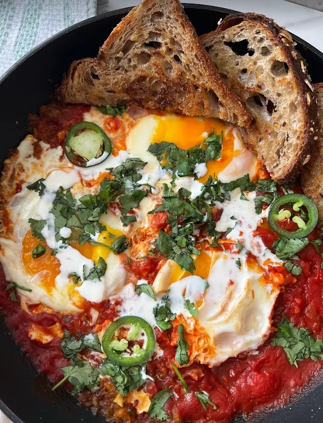 Skillet of masala shakshuka topped with cilantro and sliced jalapeño