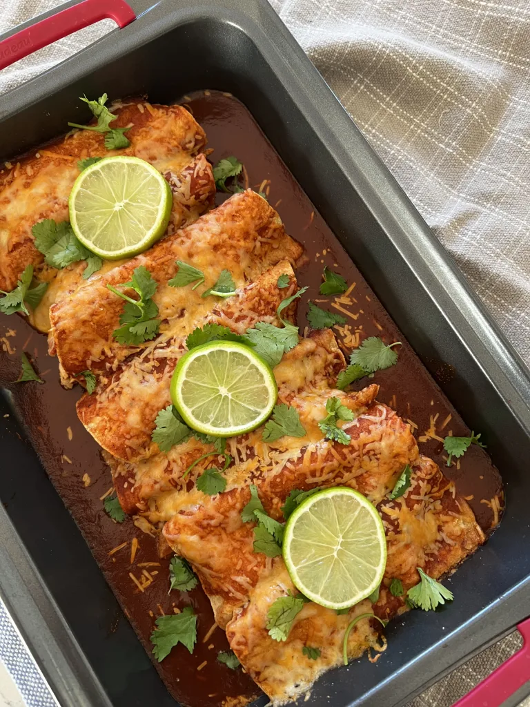 Chipotle chicken enchiladas topped with lime slices and cilantro in a baking dish